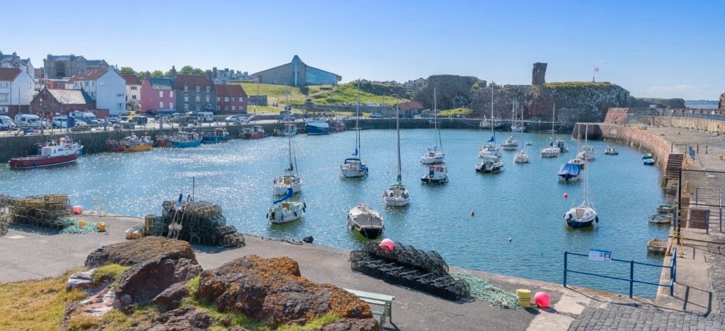 Dunbar harbour with fishing boats, creels on the quay and castle ruins on the cliff