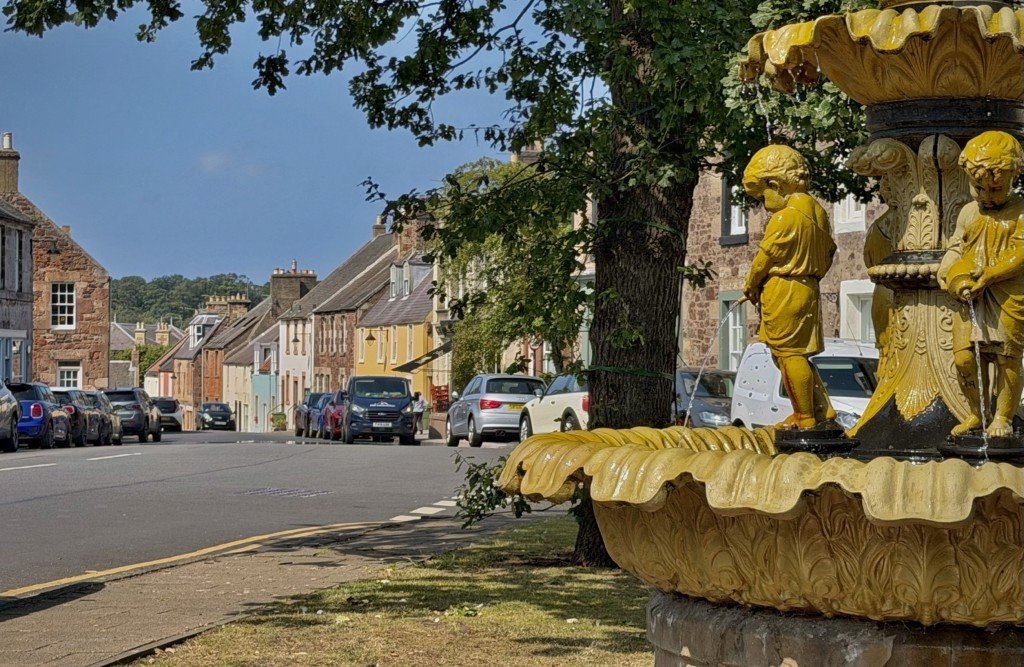 The yellow Victorian fountain on East Linton High Street with sandstone terraces beyond